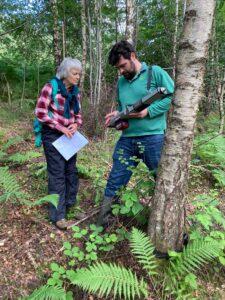 Two scientists, a man and a woman, looking at a piece of surveying equipment in woodland