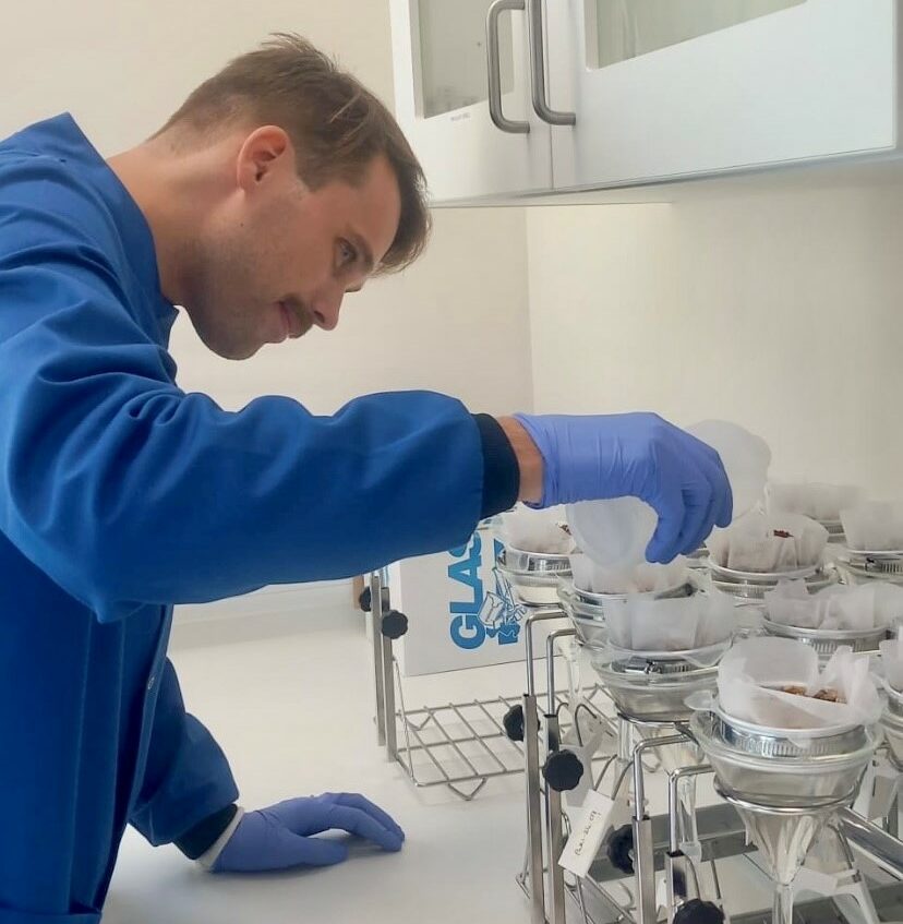 Young man in a lab coat and gloves working at a lab bench.